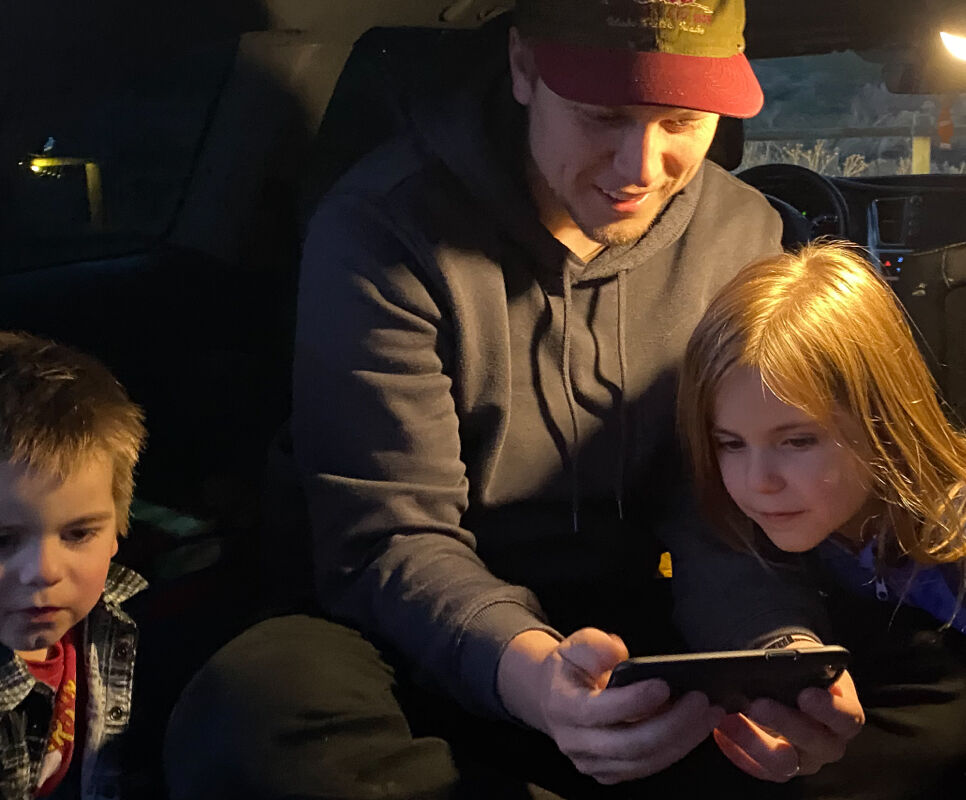 Dad watching a video on his phone with two kids using a portable lantern